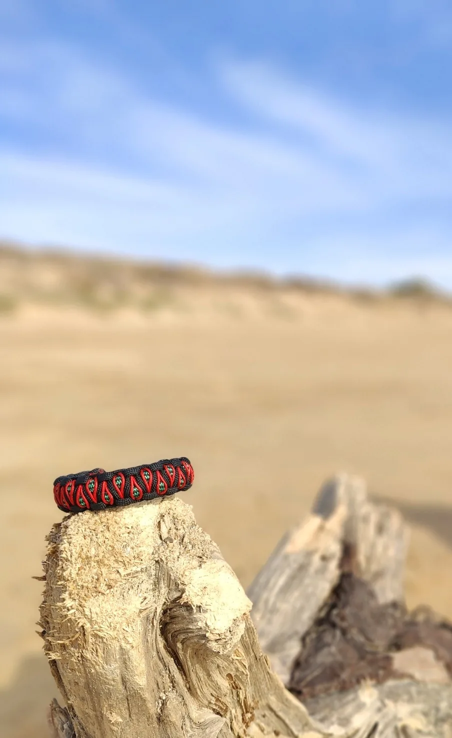 Bracelet rouge et noir en paracorde posé sur du bois flotté dans les dunes